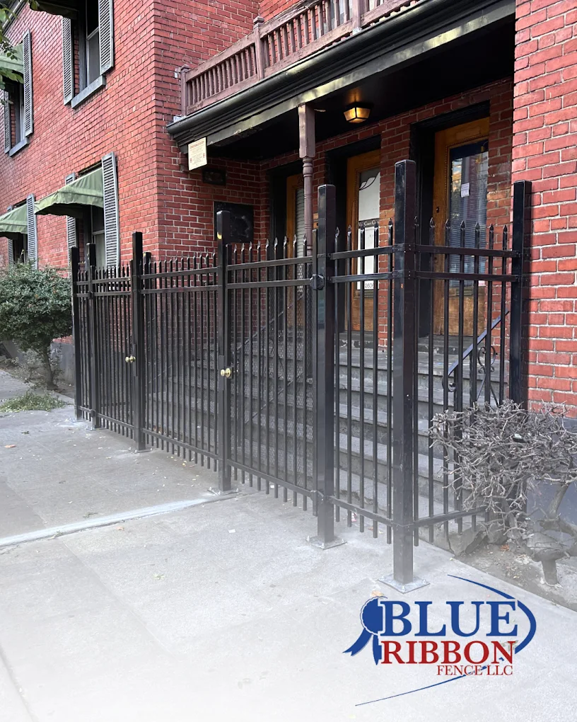 Black metal fence and matching gates at the entrance of a brick residential building.